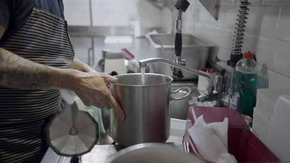 Side View of Male Chef Filling Pot with Water By Faucet in Kitchen