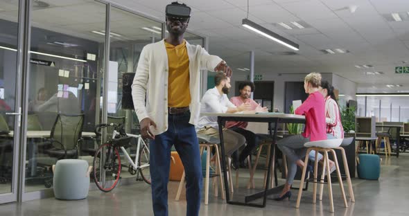 Happy african american businessman using vr headset over colleagues in office