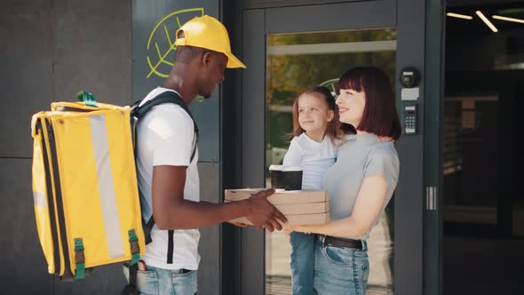 An AfricanAmerican Courier with a Thermal Bag Delivers Food and Drinks to a