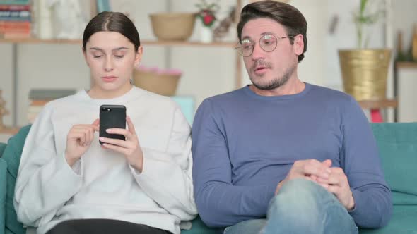 Hispanic Man Feeling Angry Near Female Partner Busy with Smartphone