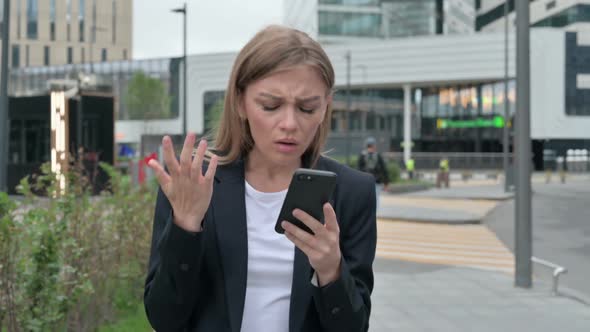 Businesswoman Reacting to Loss on Smartphone While Walking on the Street