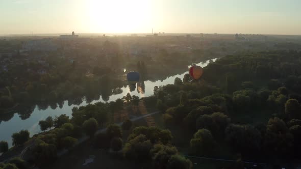 Beautiful flight at the sunrise of a red balloon over a river, forest, green trees.