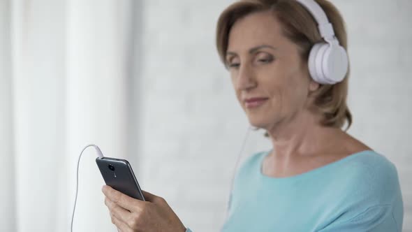 Elderly woman in Headphones scrolling screen of mobile phone, choosing song