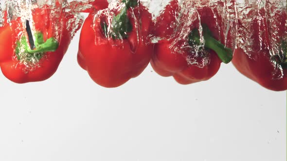 Super Slow Motion Red Pepper Falls Into the Water with Air Bubbles on a White Background