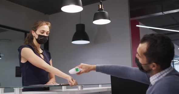 Caucasian woman in face mask has temperature checked by male colleague at office reception desk