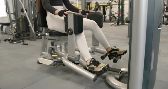 Woman Performs the Exercise of Raising the Legs in the Simulator