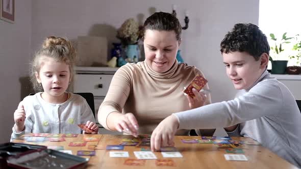 Cheerful young mother and children are playing game table. Joint games