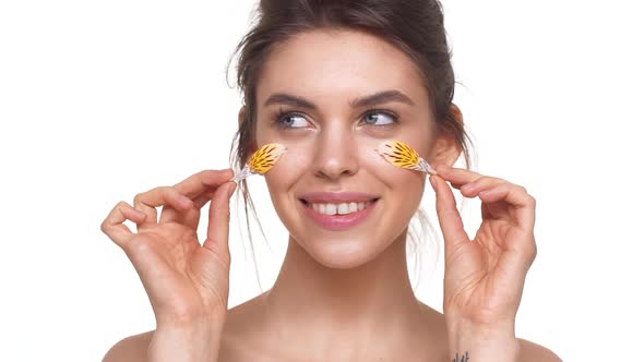 Attractive Caucasian Girl Gently Touching Face with Petals Over White Background in Slowmotion