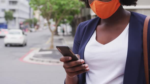 African american woman wearing face mask using smartphone in street