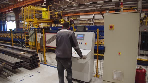 Worker in Protective Uniform Operates the Robotic Machinery Welding Steel Parts with Computer System