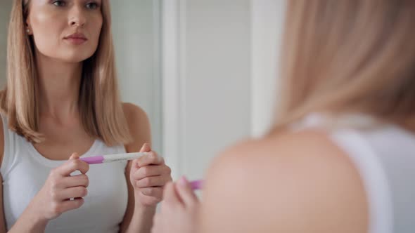 Young woman standing in front of bathroom mirror and waiting for pregnancy test results. Shot with R