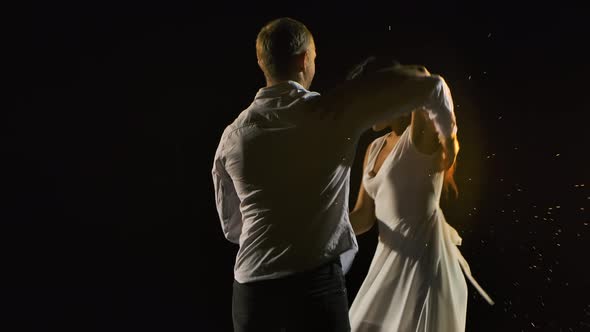 Cute Smiling Couple Dancing Salsa in a Dark Studio. A Man and a Woman in White Clothes Are Enjoying