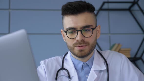 Close up view of male doctor looking at medical documentation and typing at laptop