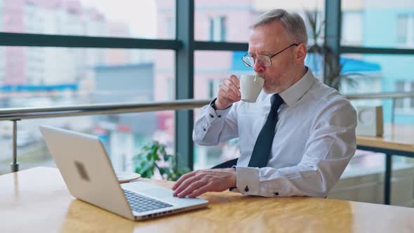 Senior man with a cup working at home on laptop
