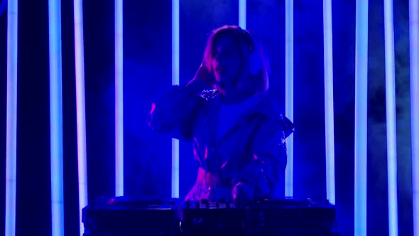 Portrait of a Young Stylish Woman in Big White Headphones Dances and Mixes Music at the DJ Turntable