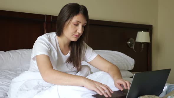 Young Woman Typing on a Laptop While Sitting in Bed Covered with a Blanket