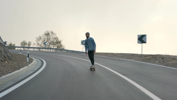 Young Man with a Beard Riding Skateboard Cruising Downhill on Countryside Road