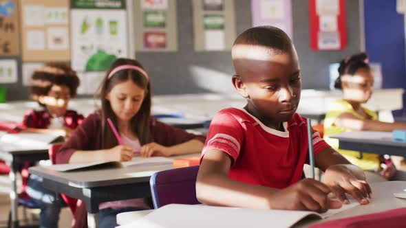 Portrait of african american schoolboy sitting in class, making notes, looking at camera