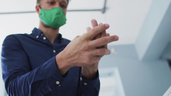 Caucasian man wearing face mask using hands sanitizer at modern office