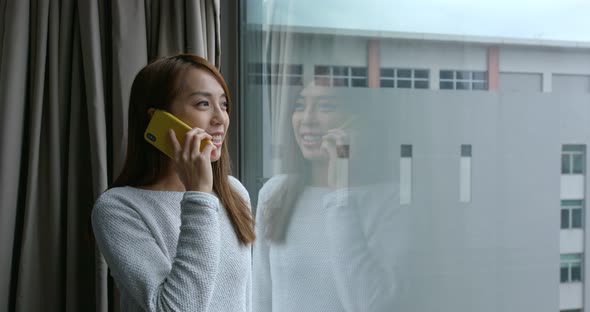 Woman chat on cellphone and stand beside the window