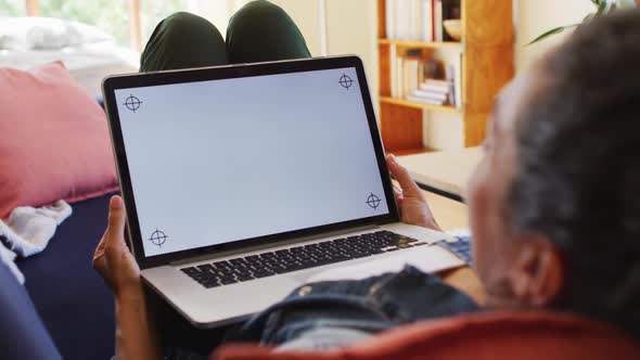 Caucasian woman using laptop on video call, lying on sofa at home