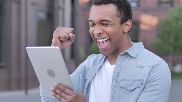 African Man Celebrating Success on Tablet Outdoor