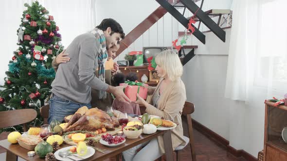 family having holiday dinner present box giving to grandmother