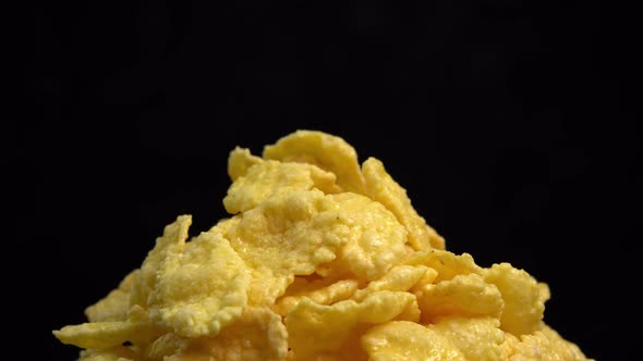 Crispy corn flakes rotating on black background close up, dry healthy breakfast. Honey cornflakes