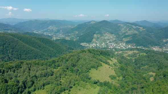 Aerial Drone View of a Village in a Mountain Valley Against a Blue Sky with Rare Clouds