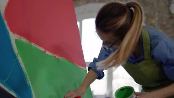 Female Artist Working with Large Paintbrush and Green Color with Her Artwork