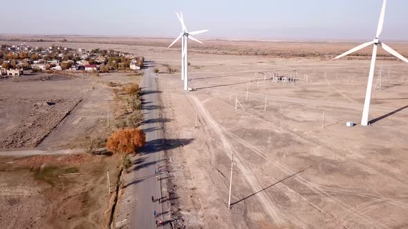 Cyclists ride along road with a view of windmills.