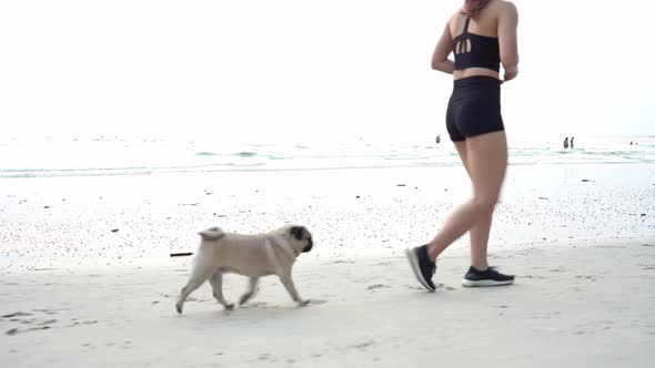 Strong woman running on sand on the Beach with dog pug breed