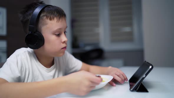 Boy eating in kitchen room. Portrait of boy using digital tablet during lunch