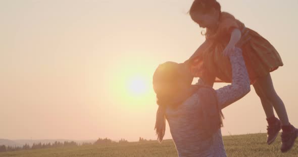 mother and young daughter walking and playing in a field during sunset