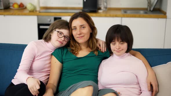 Portrait of Two Girls with Down Syndrome in Sitting on a Couch Together Embracing with Their Mom