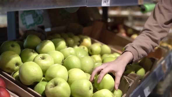 A Woman's Hands Take a Green Apple From the Shelf at the Store