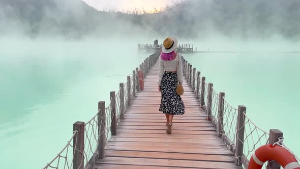 A Woman in a Hat Walks Across a Bridge on an Unusual Blue Hot Volcanic Lake