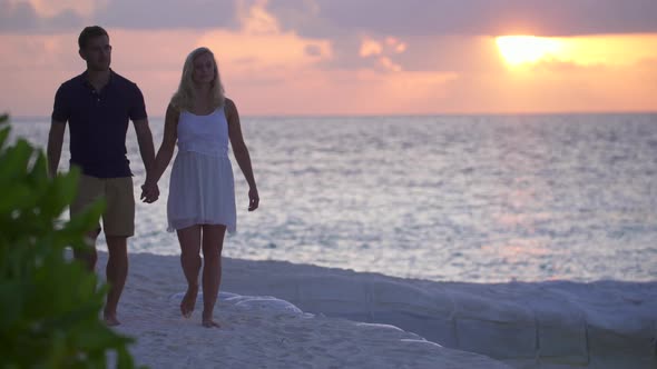 A couple walking on the beach at sunset at a tropical island resort hotel