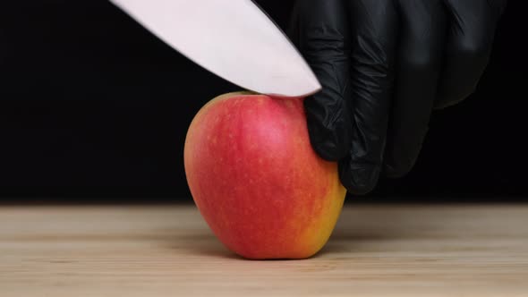 Cuts an apple in half with a knife on black background