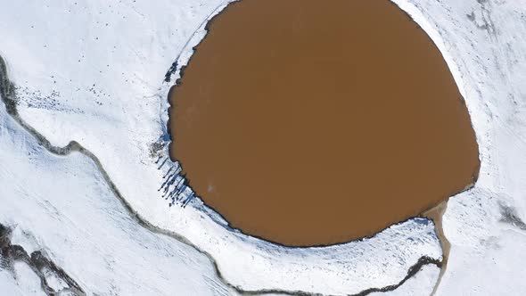 Aerial top down zoom in on a crater lake, Birkat Ram, in snow on Mount Hermon in beautiful light, Is