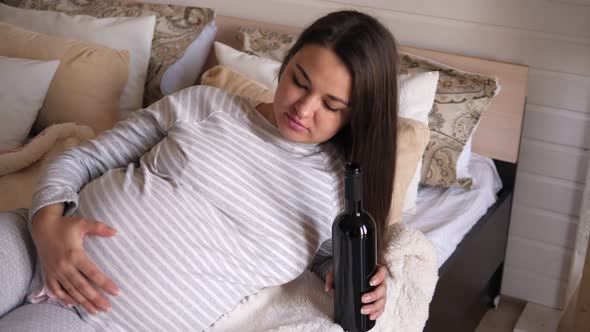 Closeup of a Pregnant Woman Lying on a Bed with a Bottle of Wine in Her Hands