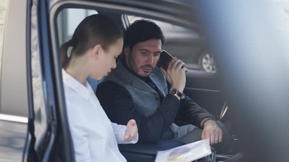 Young Intelligent Concentrated Man Listening to Smart Woman Analyzing Business Graph Sitting in Car