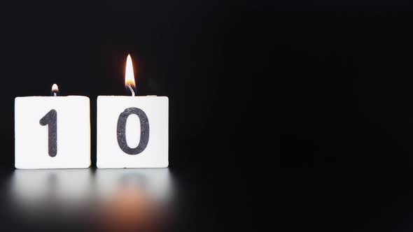 A square candle saying the number 10 being lit and blown out on a dark black background