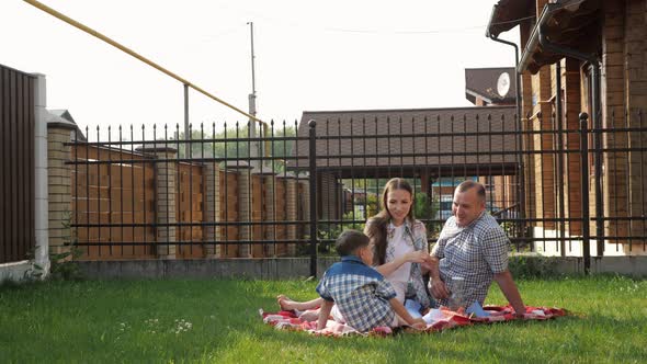 Happy Young Woman and Man Sit with Little Boy on Lawn