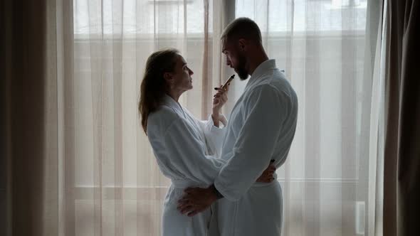 a Man and a Woman in White Coats are Standing at a Large Window and Smoking One Electronic Cigarette