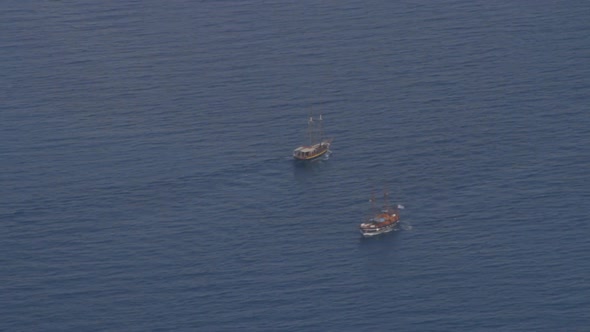 Two small excursion tourist boats cross paths in the aegean sea. As seen from the high cliffs of the