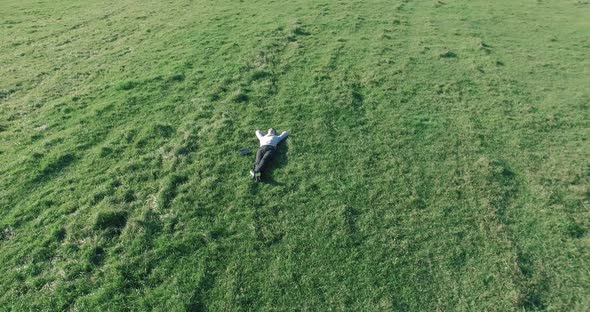 Low Orbital Flight Around Man on Green Grass with Notebook Pad at Yellow Rural Field