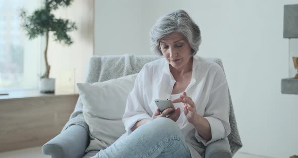 Older Middle Aged Female Looking at Smartphone Screen Watching Funny Photo or Video