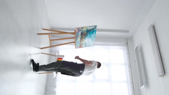 A Modern Artist Working in the Studio Emotionally Paints on a Large White Canvas with a Brush