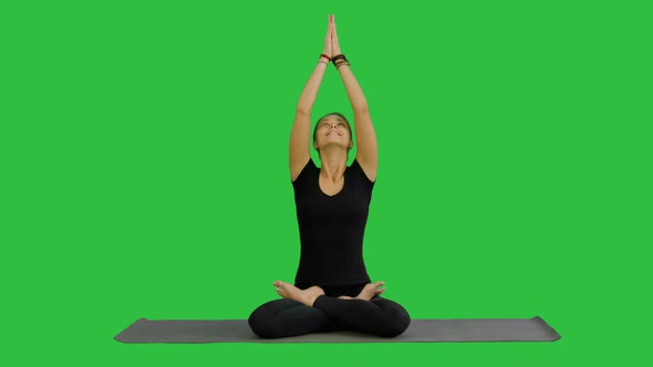 Young Woman Practicing Yoga, Sitting in a Lotus Position, Meditating with Closed Eyes on a Green